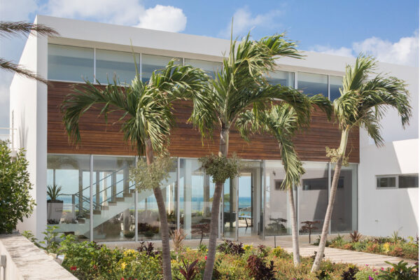 Exterior view of Champagne Shores Villa, featuring modern architecture, large windows, and a beautifully landscaped garden with palm trees.